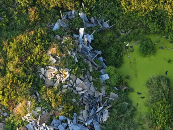 Aerial photo of scrap metal and rubble at the edge of a neon green pond with tires floating in it